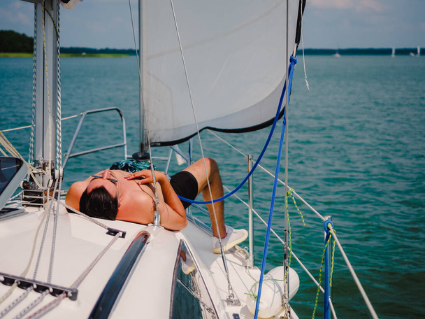 young person sunbathing on a sailboat under the sail - Φωτογραφία, εικόνα