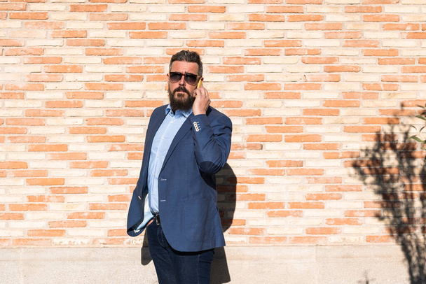 Businessman in sunglasses talking on the phone while standing outdoors on the street. - Foto, Bild