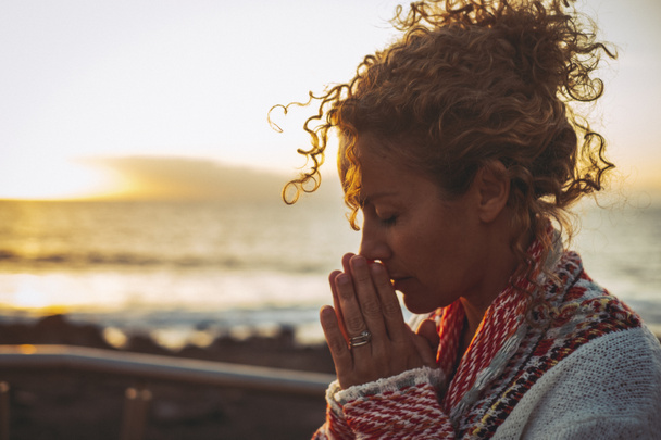 Meditazione ed equilibrio interiore concetto di felicità interiore con ritratto laterale di giovane donna che prega e medita all'aperto con oceano tramonto sullo sfondo. Concetto di stile di vita di salute mentale - Foto, immagini