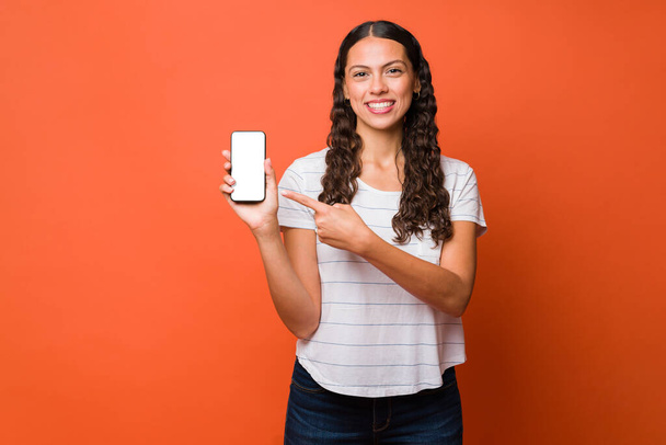 Hymyilevä latino nuori nainen osoittaa älypuhelimeen, kun käytät uutta hauskaa sovellusta - Valokuva, kuva