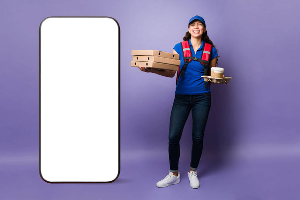 Super onnellinen toimitus henkilö nauraa kuljettaessaan pizzaa ja kahvia asiakkaalle työskennellessään elintarvikkeiden toimitus app - Valokuva, kuva