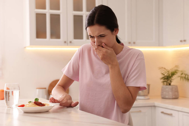 Young woman feeling nausea while seeing food at table in kitchen - Valokuva, kuva