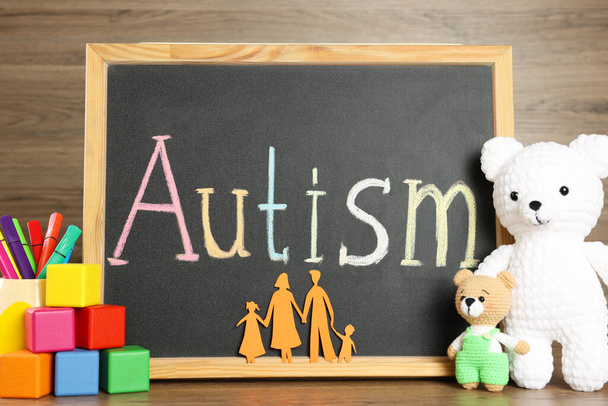 Chalkboard with word Autism, paper cutout of family and different toys on wooden table - 写真・画像