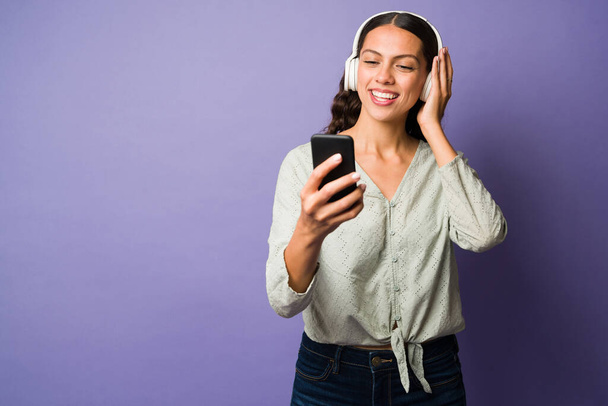 Mujer latina alegre le encanta escuchar música con auriculares. Hermosa mujer usando una aplicación para disfrutar de la música en su teléfono inteligente - Foto, imagen