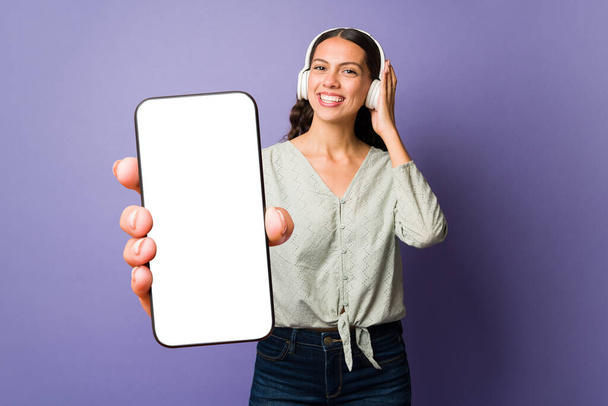 Entspannte junge Frau hört Musik mit Kopfhörern, während sie eine Musik-App auf ihrem Handy nutzt - Foto, Bild