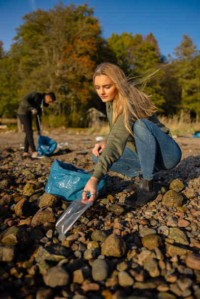 Poważna młoda kobieta w zespole ochrony środowiska zbiera plastik na plaży - Zdjęcie, obraz