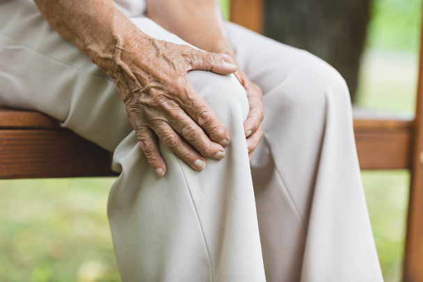 Senior woman sitting on bench, holding her painful knee - Foto, Bild