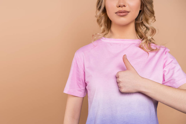 partial view of young woman in t-shirt showing thumb up isolated on beige - Foto, Bild