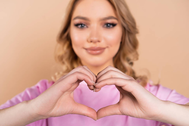 smiling woman showing heart sign with hands on blurred background isolated on beige - Foto, Imagem