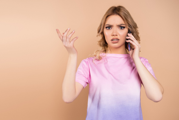 displeased woman calling on smartphone and pointing with finger isolated on beige - Foto, Imagen