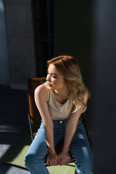 pretty woman with wavy hair sitting on chair and looking away on blurred foreground - Foto, immagini