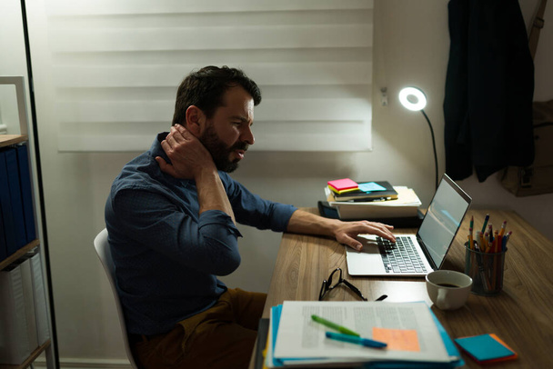 Profil eines gestressten jungen Mannes mit Nackenschmerzen wegen schlechter Körperhaltung beim Sitzen am Schreibtisch  - Foto, Bild