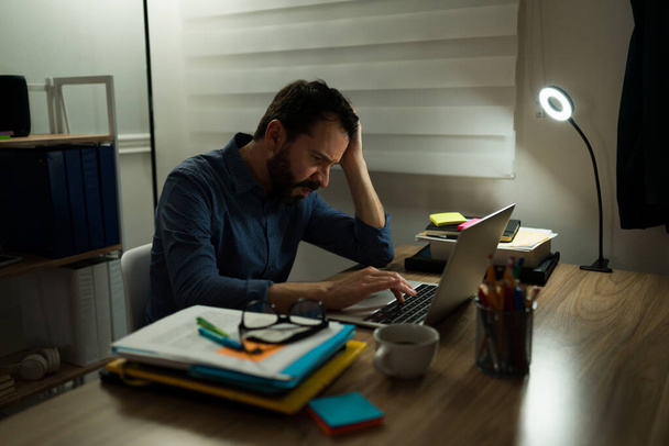 Sad stressed man feeling very tired while overworking. Exhausted man working late at night at the office - 写真・画像