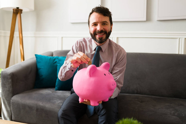 Financial freedom concept. Handsome wealthy man with a lot of money using a piggy bank for his savings - Photo, Image