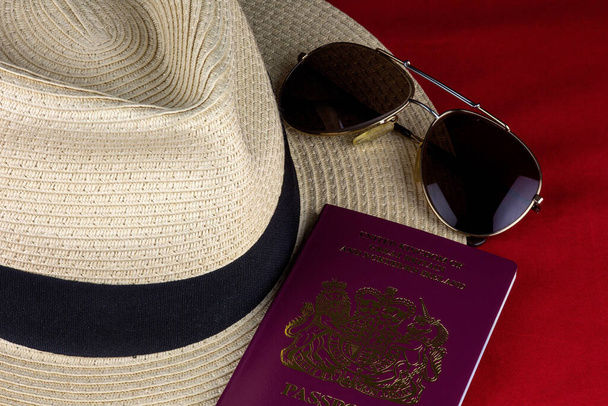 Καπέλο άχυρο με διαβατήριο και sungtlasses σε κόκκινο φόντο - Φωτογραφία, εικόνα