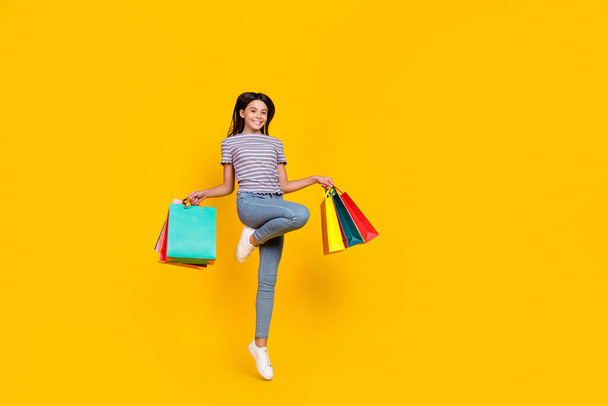 Full length photo of young girl jump shopping store holiday present isolated over yellow color background - Photo, Image