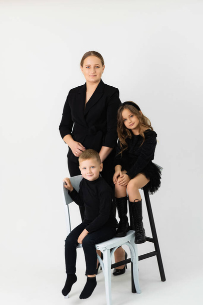 Mamá con hijo e hija en ropa negra en el estudio. Retrato familiar - Foto, Imagen
