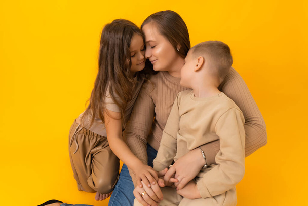 Нежный семейный портрет матери, дочери и сына на жёлтом фоне в студии  - Фото, изображение