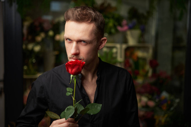 Serious ready for date macho man in black shirt with red rose - Foto, Imagen