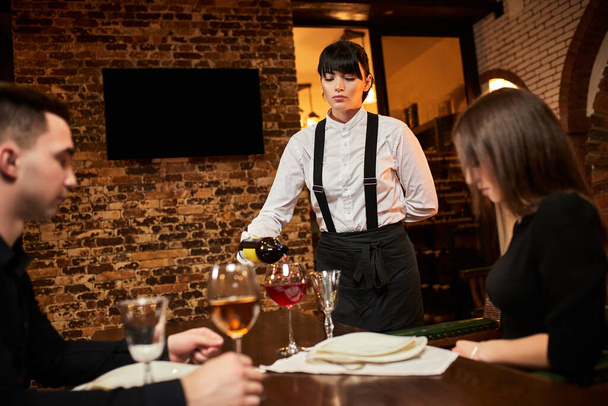 The waiter in uniform pours visitors wine in restaurant - Foto, Bild