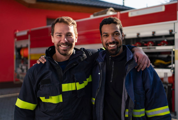 Happy firefighters crew with fire station and truck in background looking at camera. - Fotografie, Obrázek