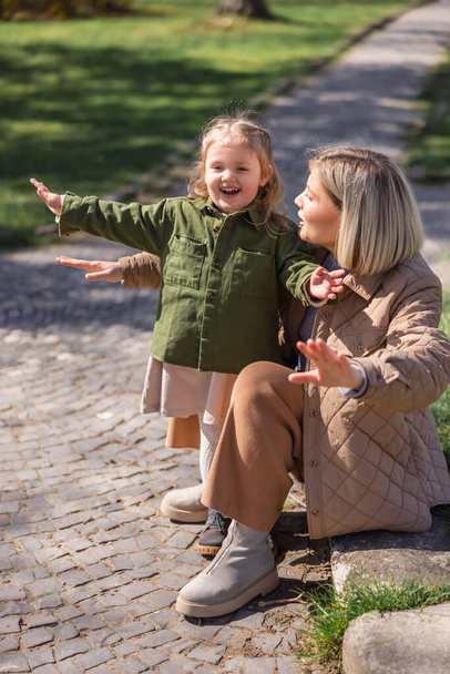 excitada madre e hija con las manos extendidas divirtiéndose en el parque - Foto, Imagen