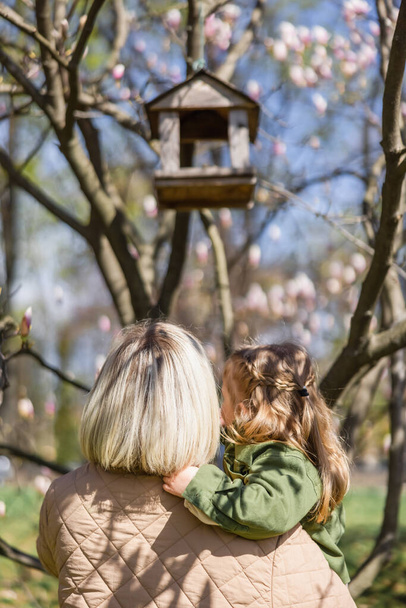 back view of mother and daughter near blurred birdhouse in park - Photo, Image