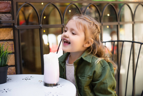 Mutlu çocuk dışarıdaki lezzetli milkshake bardağında samana uzanıyor. - Fotoğraf, Görsel