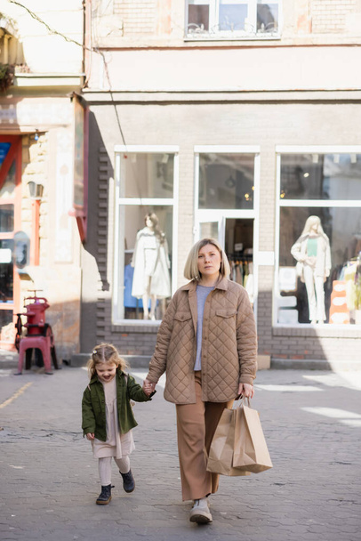 täyspitkä näkymä nainen ostoskassit kädestä onnellinen tytär kävellessään ulkona - Valokuva, kuva
