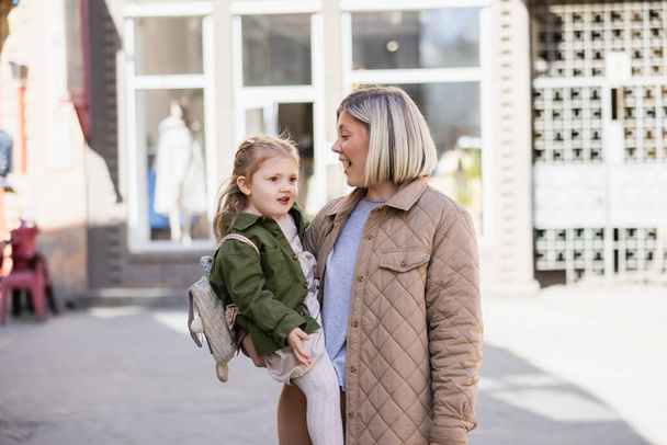 verbaasd blond vrouw holding weinig dochter op stad straat - Foto, afbeelding