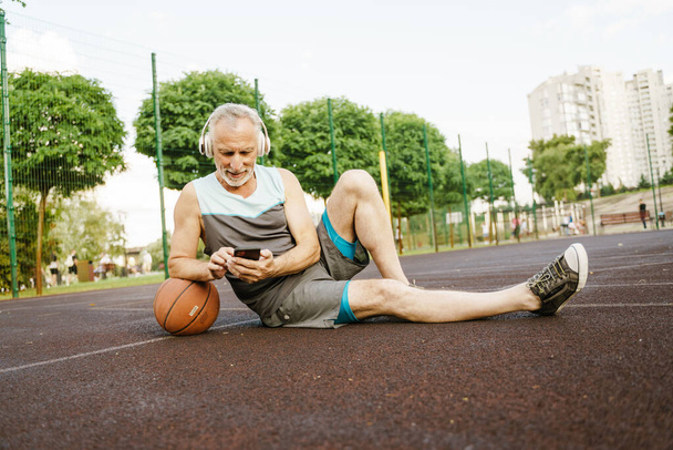 Szürke férfi zenét hallgat és mobilt használ, miközben a játszótéren ül - Fotó, kép