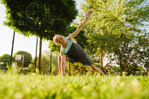 Grey senior sportsman listening music during yoga practice in green park - Foto, Imagen