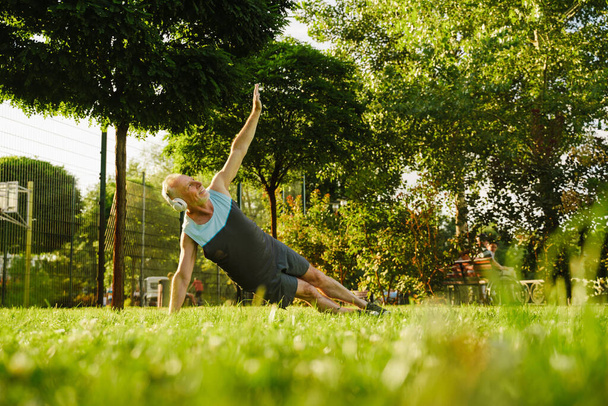 Grey senior sportsman listening music during yoga practice in green park - Foto, Bild
