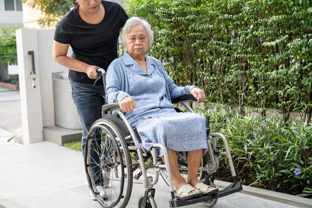 Pflegerin hilft und pflegt asiatische Seniorin oder ältere Patientin im Rollstuhl auf Rampe der Krankenstation, gesundes starkes medizinisches Konzept - Foto, Bild
