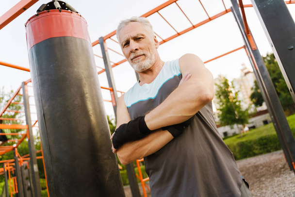Grey senior man in boxing bandage working out on sports ground - Foto, afbeelding