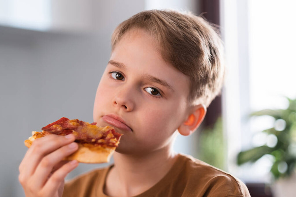 Θλιβερό αγόρι απολαμβάνοντας το φαγητό νόστιμα πίτσα στο σπίτι. - Φωτογραφία, εικόνα