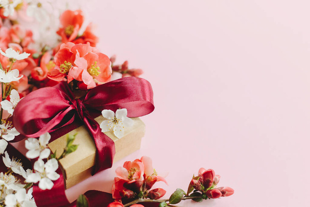 Fijne Moederdag. Stijlvolle geschenkdoos met bloemen op roze achtergrond. Wenskaart template met ruimte voor tekst. Ambachtelijke gift met lint, rode bloemen en kersenbloesem. Ansichtkaart voor vrouwen - Foto, afbeelding