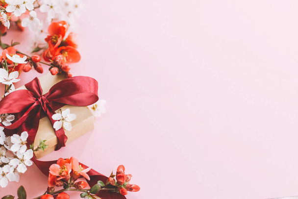 Feliz Dia das Mães. Caixa de presente elegante com flores sobre fundo rosa. Modelo de cartão de saudação com espaço para texto. Presente de artesanato com fita, flores vermelhas e flor de cereja. Cartão postal de dia de mulher - Foto, Imagem