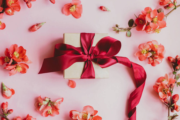 Hyvää äitienpäivää. Tyylikäs lahjapaketti kukkia vaaleanpunainen tausta tasainen lay. Tervehdyskortin malli. Juhlava koostumus veneen lahja nauha ja punaiset kukat. Naisten päivä tai syntymäpäivälippu - Valokuva, kuva