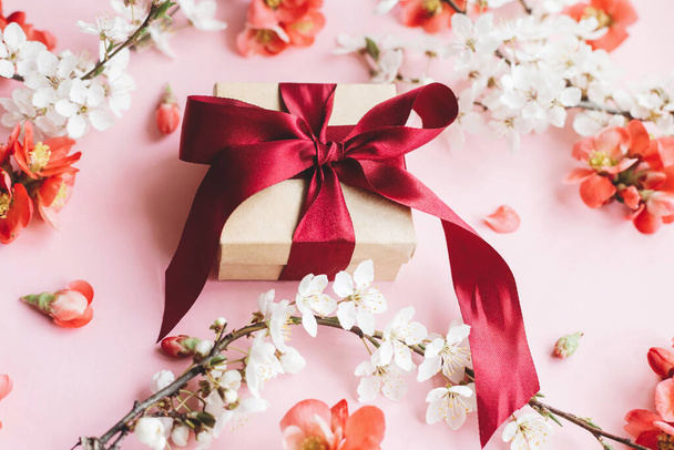 Hyvää äitienpäivää. Tyylikäs lahjapakkaus, jossa on kukkia vaaleanpunaisella taustalla. Tervehdyskortin malli. Craft lahja nauha, punaisia kukkia ja kirsikankukka. Naisten päivä - Valokuva, kuva
