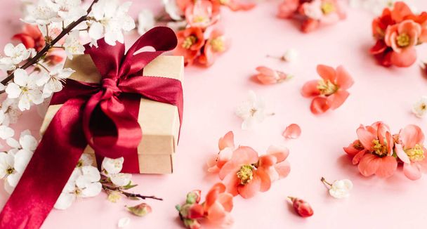 Stylowe pudełko z kwiatami na różowym tle kompozycji. Szczęśliwego Dnia Matki. Szablon karty okolicznościowej. Rzemiosło prezent z wstążką, czerwone kwiaty i kwiat wiśni. Dzień Kobiet - Zdjęcie, obraz