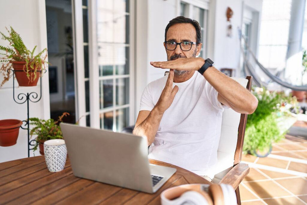 Orta yaşlı bir adam evde bilgisayar kullanıyor. El kol hareketleri yapıyor, hayal kırıklığına uğramış ve ciddi bir yüz ifadesi takınıyor.  - Fotoğraf, Görsel