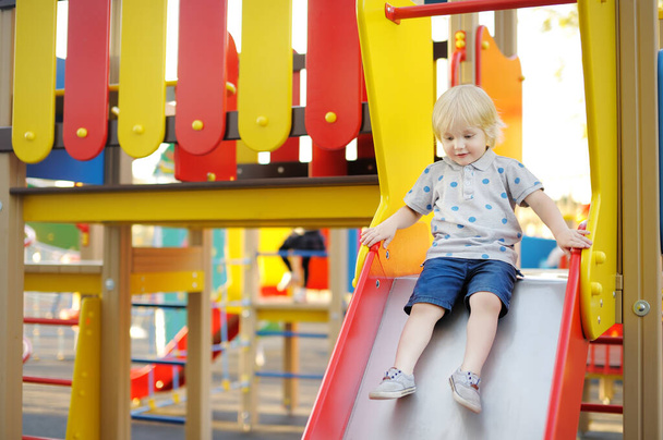 Cute toddler boy having fun on slide on playground. Active summer outdoors games for little children - Foto, Imagem