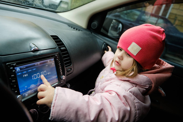 Mała dziewczynka zmieniająca stację radiową słuchając muzyki w samochodzie. Słuchanie radia w samochodzie. Muzyka automatyczna - Zdjęcie, obraz
