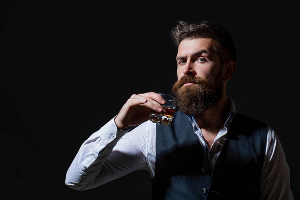 Zarif takım elbiseli sakallı bir işadamı ve bir bardak viski. Degukasyon, tatma. Sakallı adam elinde brendi bardağı tutuyor. Tatma ve degukasyon konsepti - Fotoğraf, Görsel