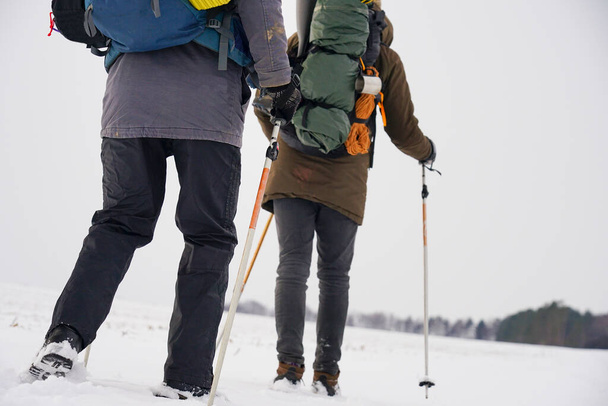 Two men in  winter gear are walking through the snow. Winter expedition to the checked pole. A man carries a large backpack - Foto, Imagen