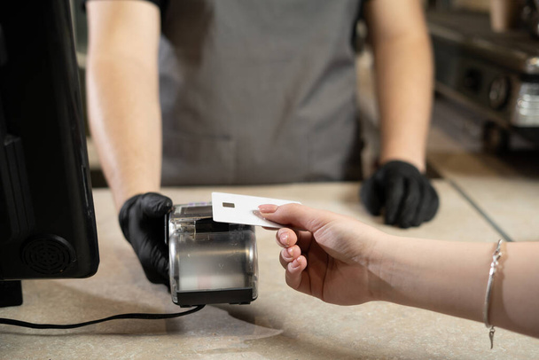 Contactless payment concept, woman customer holding credit card near nfc technology on counter, customer pays transaction on cashier rfid terminal in restaurant store, closeup view - Foto, Imagem