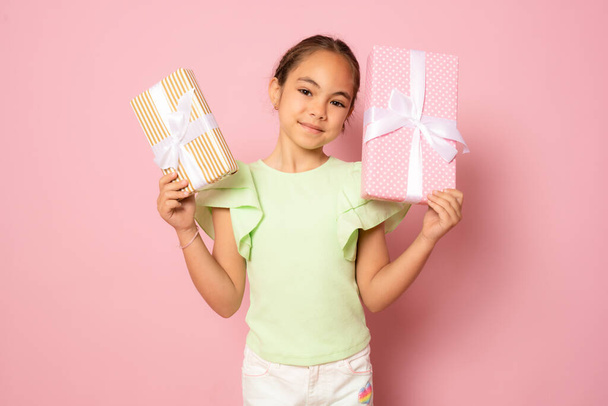 Портрет милой красивой маленькой девочки, стоящей изолированно на розовом фоне, держа подарочные коробки - Фото, изображение