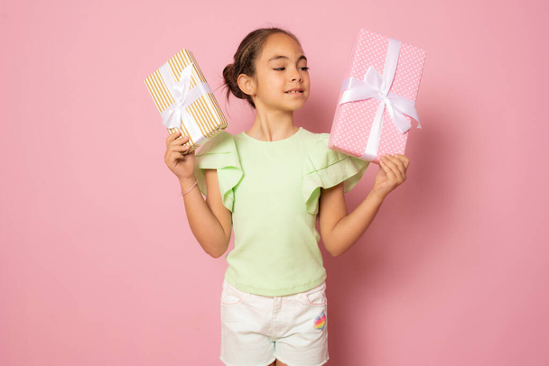 Portrait of a lovely beautiful little girl standing isolated over pink background, holding gift boxes - Fotó, kép