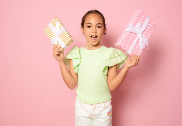 Πορτρέτο ενός όμορφου μικρού κοριτσιού που στέκεται απομονωμένο σε ροζ φόντο, κρατώντας κουτιά δώρων - Φωτογραφία, εικόνα